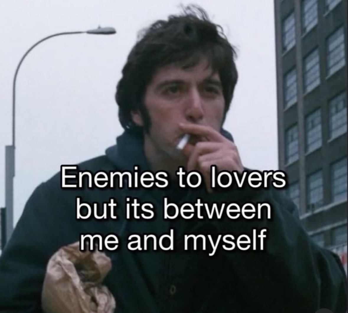 A meme featuring a still image of actor Sylvester Stallone as the character Rocky Balboa. He is shown from the chest up, wearing a dark jacket, looking somewhat weary, and smoking a cigarette. In the background, there is a street lamp, a grey sky, and a tall building. Overlaid on the image is white text with a black outline that reads: 'Enemies to lovers but its between me and myself'.