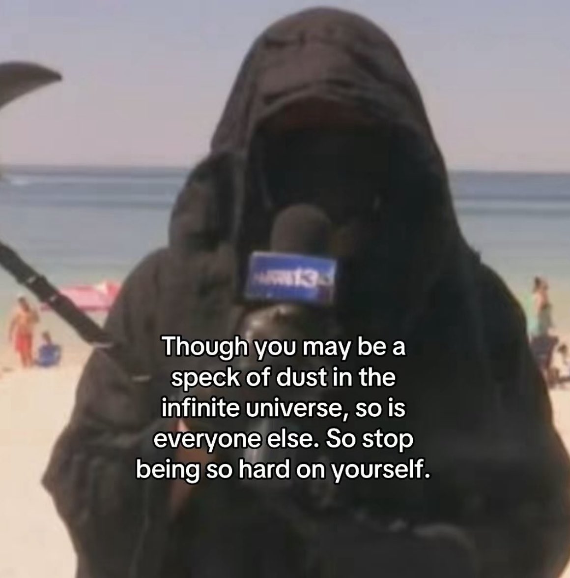 A meme featuring a person dressed as the Grim Reaper, wearing a black hooded cloak and holding a scythe, appearing as if they are being interviewed with a microphone held in front of them. The background shows a sunny beach with sand, ocean waves, and people in the distance. Overlaid text provides a philosophical, comforting message.