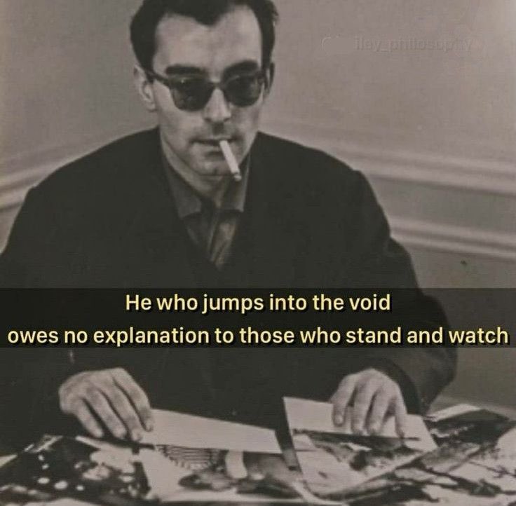 A black and white, vintage-style photograph of a man with dark hair wearing sunglasses and a dark jacket. He is sitting at a desk with papers in front of him and has a cigarette in his mouth. Superimposed over the middle of the image is a quote in white text. There is a faint watermark in the upper right corner.