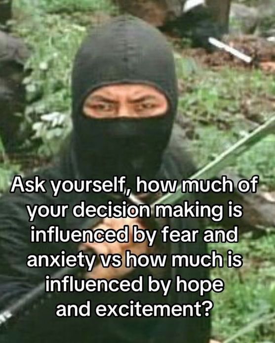 A meme featuring a person wearing a black balaclava or ninja mask, looking directly at the camera with a serious expression. The background appears to be a blurred outdoor setting with greenery. Overlaid on the image is white text providing a motivational or introspective question.