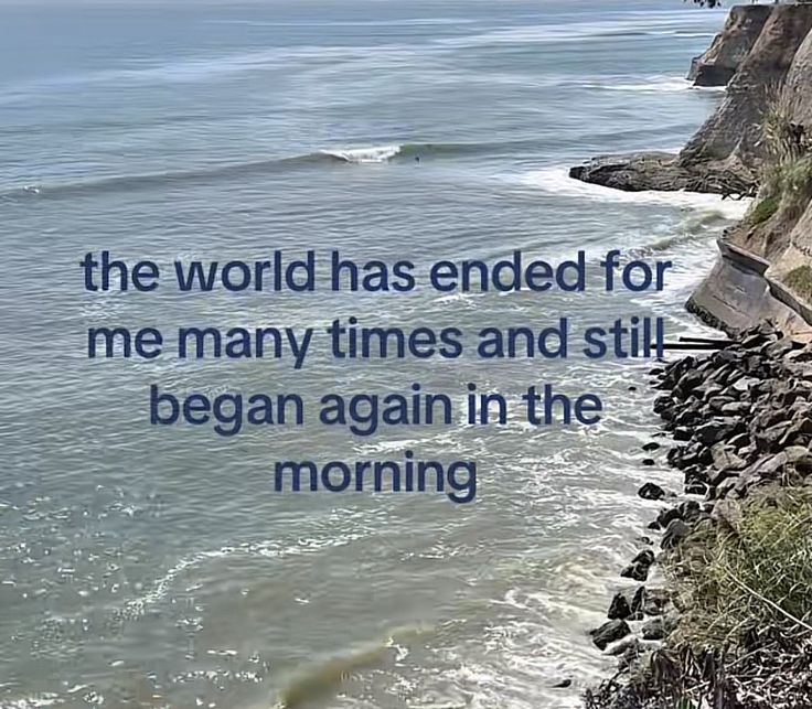 A scenic view of an ocean coastline. The image shows waves washing up against a rocky shore and a steep cliffside on the right. Overlaid on the center of the image is blue-colored text. The lighting suggests it is daytime with slightly overcast or hazy conditions.