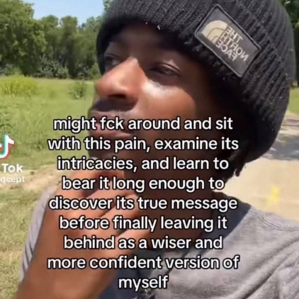 A close-up, low-angle shot of a Black man wearing a black North Face beanie. He is looking off to the side with a thoughtful or pensive expression. The background is a blurred outdoor setting with green grass and trees under daylight. Overlaid on the image is a large block of white text expressing a philosophical sentiment about processing pain, along with a TikTok watermark on the left side.