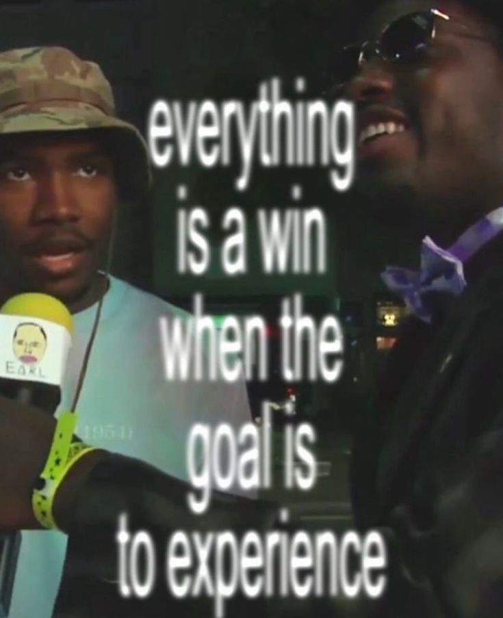 A low-light, slightly blurry vertical image featuring two men. On the left, a man wearing a camouflage bucket hat and a light blue t-shirt looks towards the camera with a neutral expression. He is holding a microphone with a yellow top that has a small logo of a face and the word 'EARL' on it. On the right, another man is visible in profile, smiling, wearing dark sunglasses and a purple bow tie. Large white text with a black outline is overlaid on the center of the image.