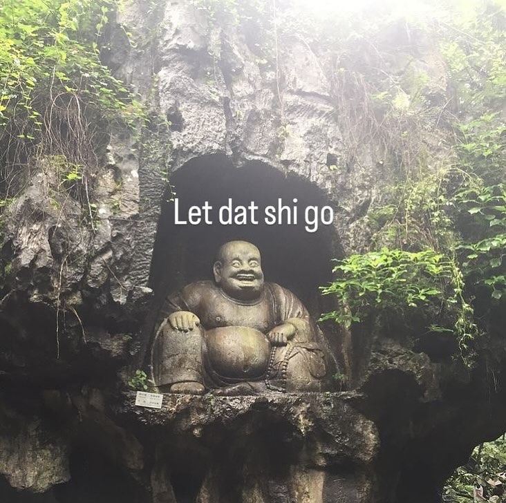 A photograph of a large, seated stone statue of a smiling, laughing Buddha (Budai) positioned within a natural rock alcove or cave. The statue is depicted with a large belly and a joyful expression. The surrounding environment is lush with green foliage, vines, and moss-covered rocks, creating a forest-like setting. White text is overlaid on the center of the image.