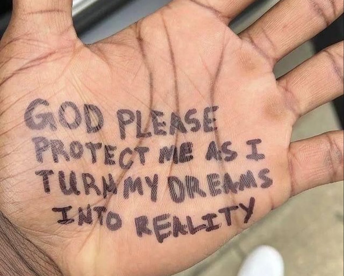 A close-up photograph of a person's open palm. Written on the palm in dark ink is a handwritten prayer or affirmation. The skin shows natural lines and textures, and the background is slightly out of focus.