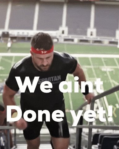 A short video clip shows a muscular man in a black t-shirt and a red headband performing a heavy exercise, likely a squat or a lift, in what appears to be an outdoor athletic stadium. Large white text overlays the center of the screen reading 'We aint Done yet!'