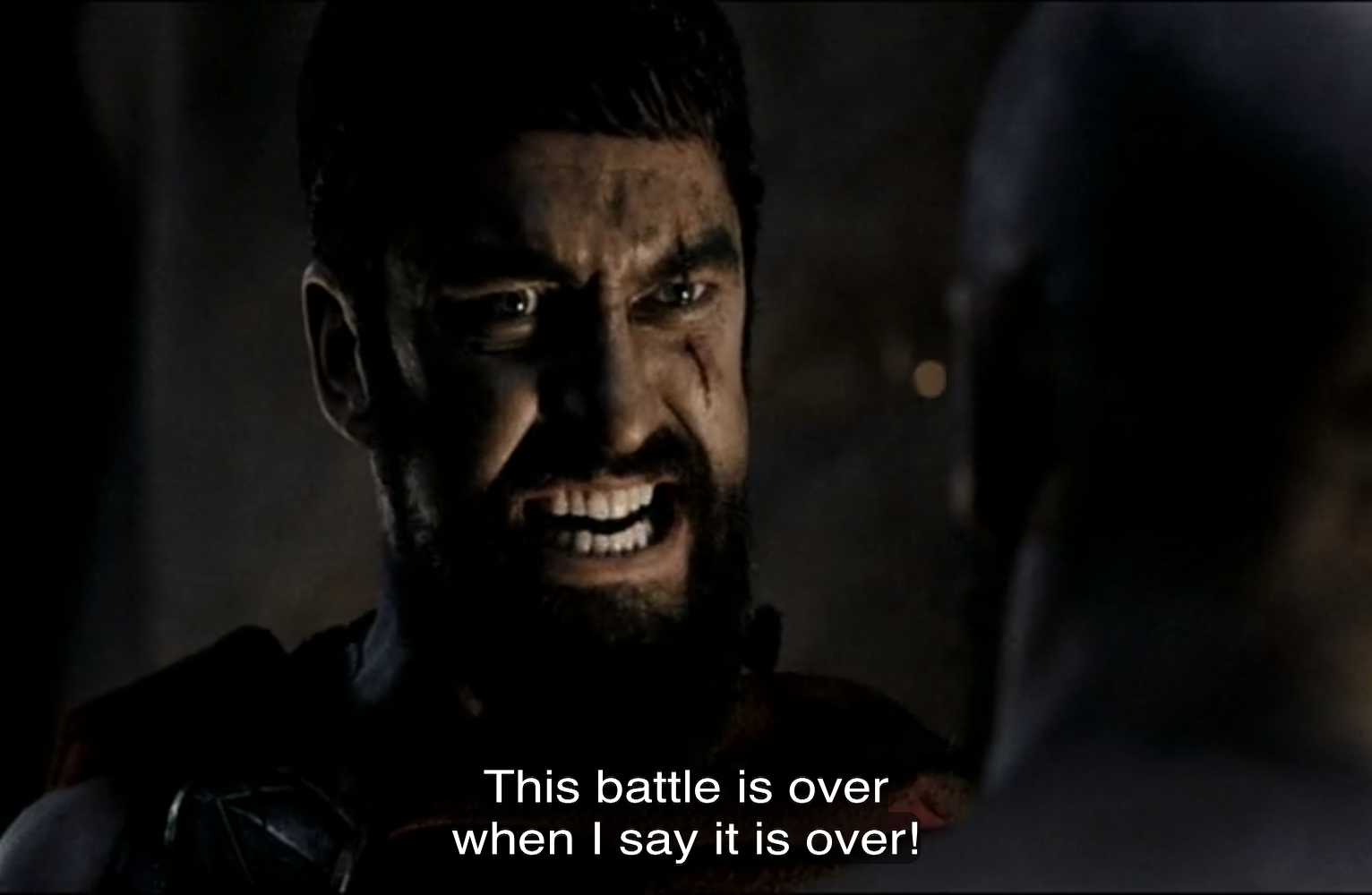 A close-up shot of a man with dark hair and a beard, appearing intense and angry, with clenched teeth and a visible scar on his cheek. He is partially in shadow, suggesting a dramatic or cinematic setting. In the foreground, the blurred back of another person's head is visible. White subtitle text at the bottom of the image reads, 'This battle is over when I say it is over!'
